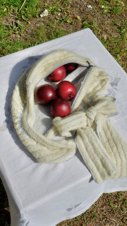 Yellow knitted scarf with red plums on a white cloth outdoors.
