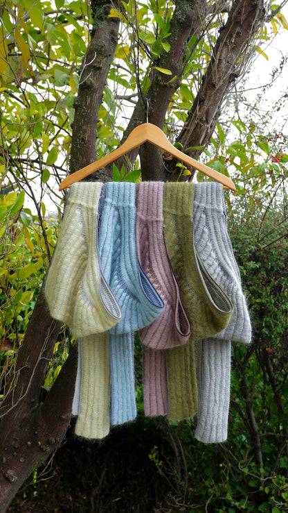 Knitted scarves in various colors hanging on a wooden hanger against a natural background.